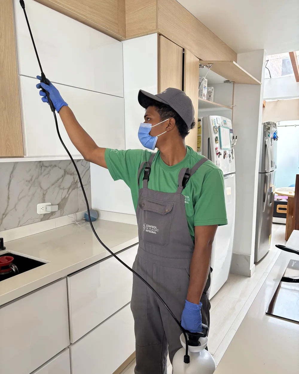 Técnico de CPI aplicando control de plagas en la cocina de un domicilio, con equipo de protección